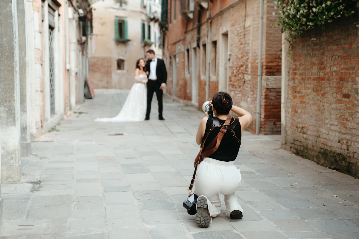 Photographe à genoux qui photographie des mariés dans une ruelle pavée