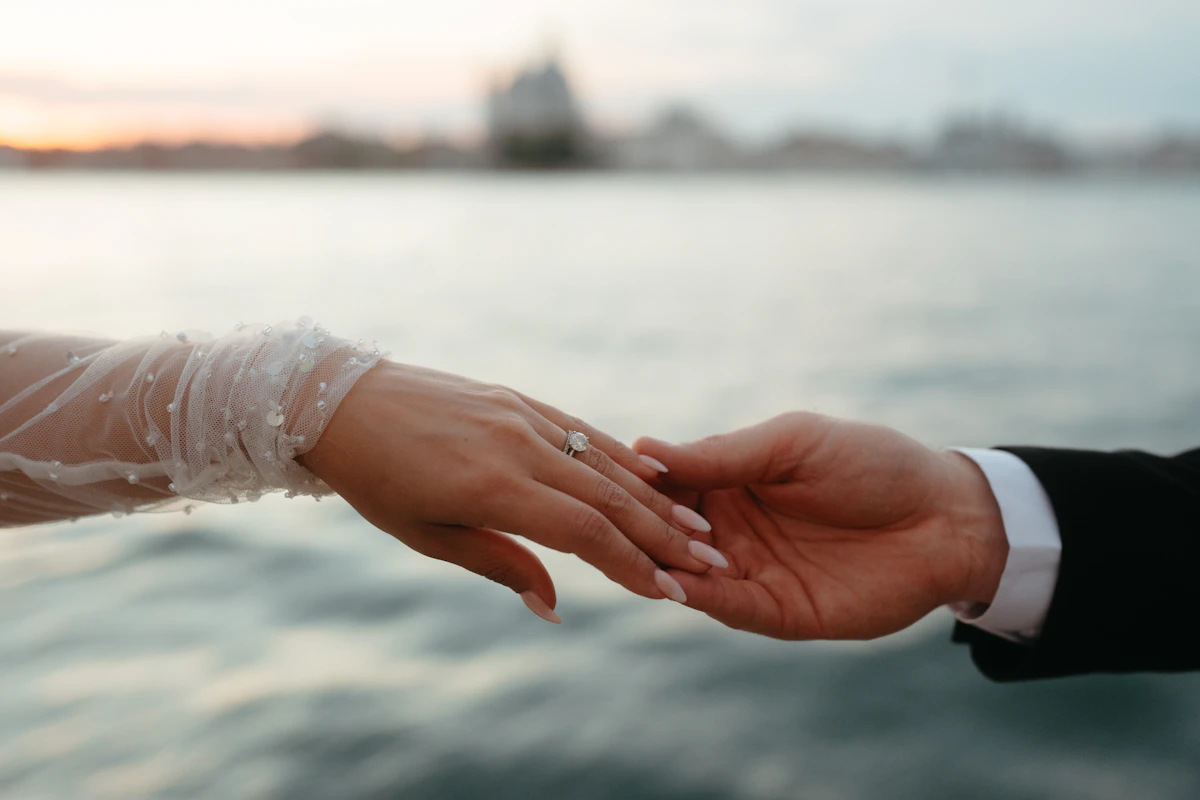 Main de la mariée, bague au doigt, posée dans celle du marié au bord de l’eau