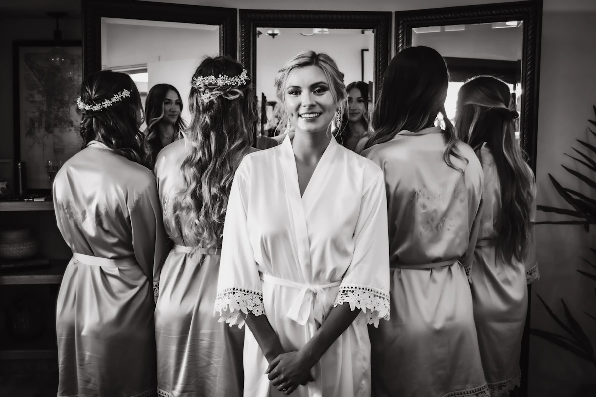 Mariée en peignoir entourée de ses témoins devant des miroirs, en noir et blanc