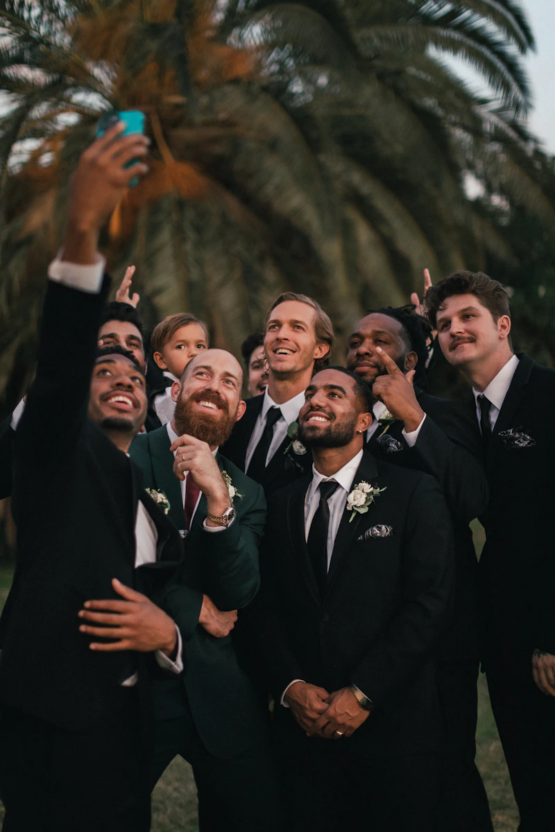 Marié et ses témoins en costume qui font un selfie sous un palmier