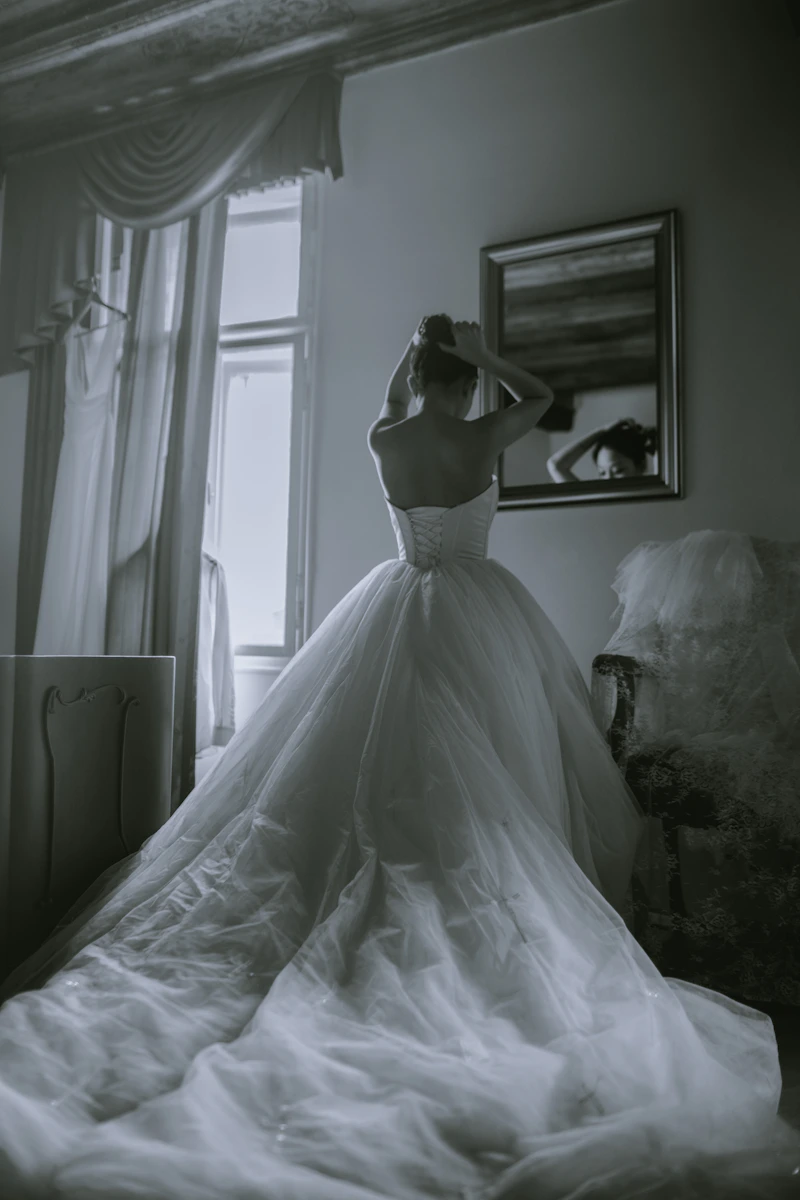 Mariée en robe à traîne face à un grand miroir, en noir et blanc