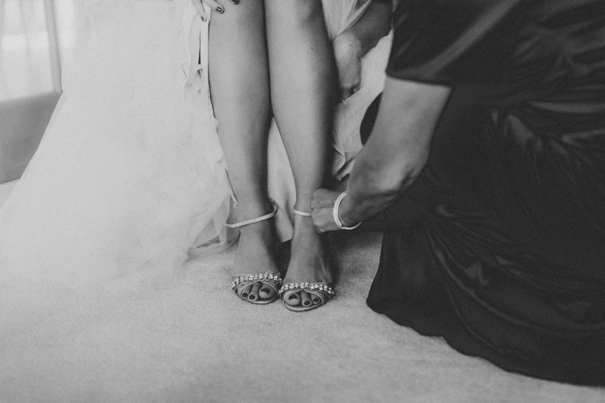 Proche qui attache les sandales de la mariée, en noir et blanc