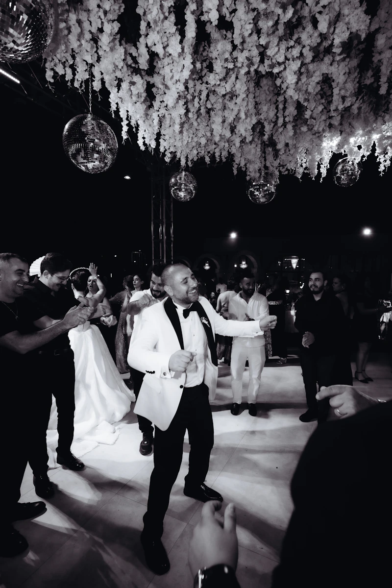 Marié en smoking blanc qui danse sous un plafond de fleurs et de boules à facettes, en noir et blanc