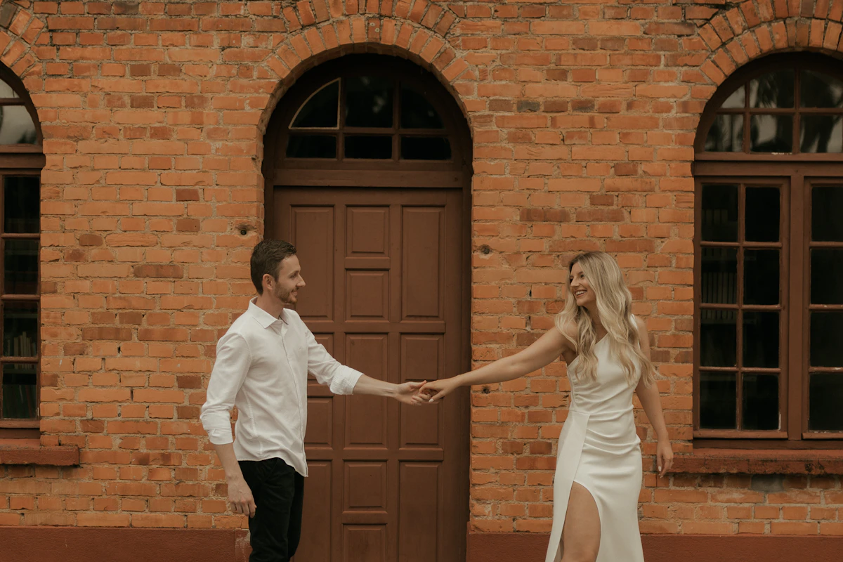 Couple main dans la main devant une façade en briques et une porte en bois