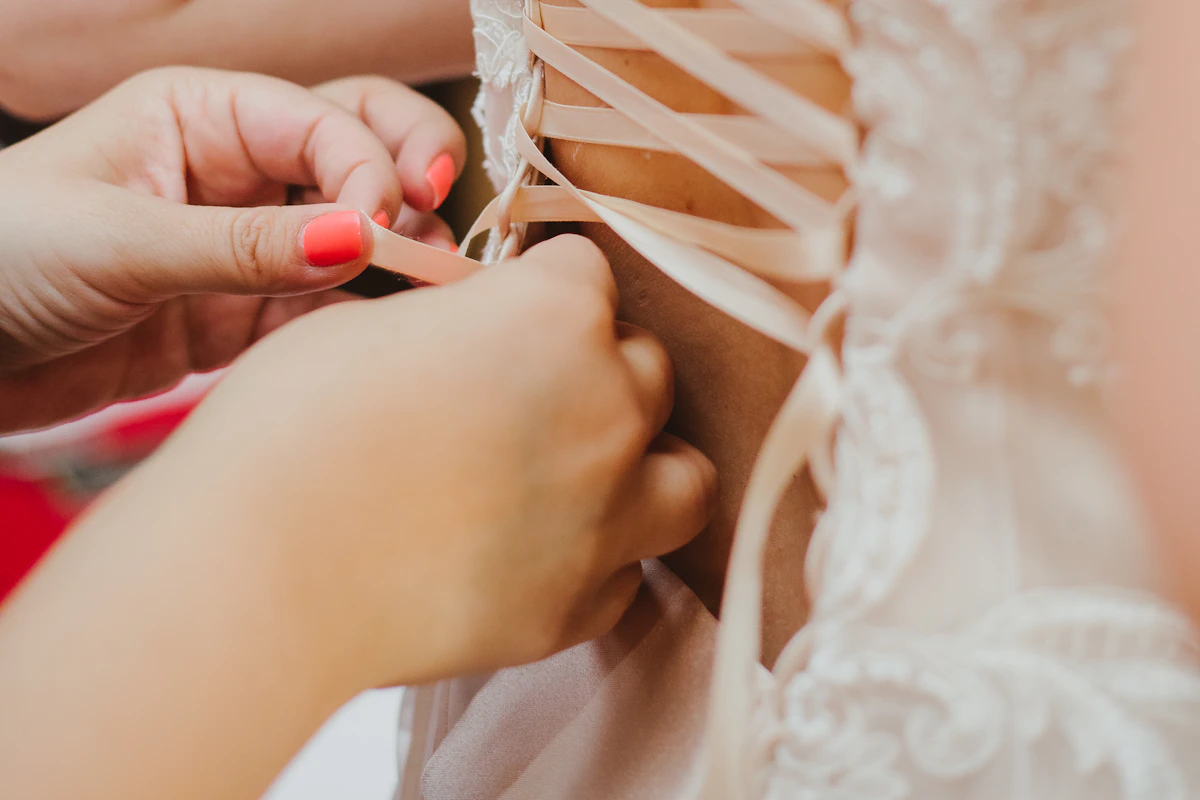 Mains qui lacent le corset de la robe de la mariée pendant les préparatifs