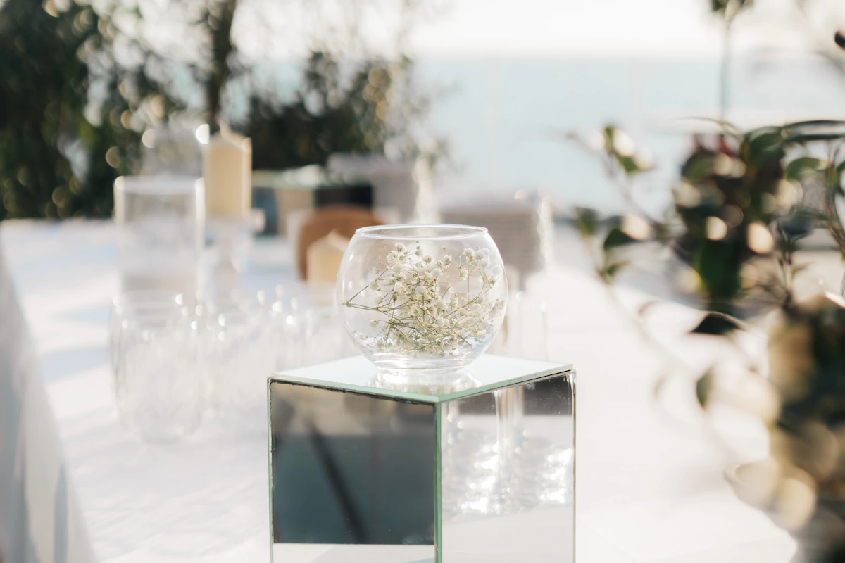 Table de réception blanche face à la mer, vase de gypsophile sur un cube miroir